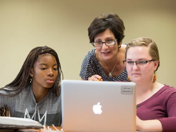 Three women surrounding a laptop looking something up