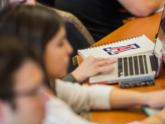 Students typing on the laptop with a UA notebook nearby