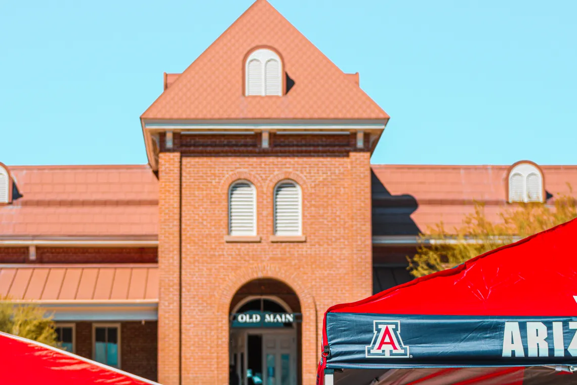 Old Main with a tent in front of it that has the UofA logo on the corner