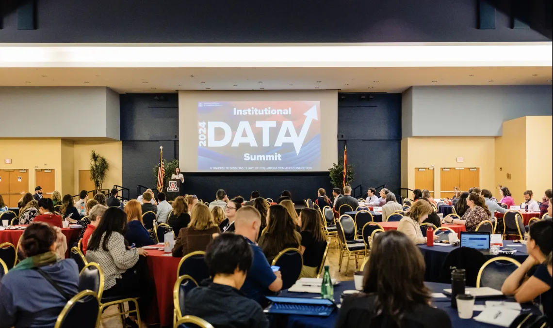 Student Union Grand Ballroom filled with people at tables and a powerpoint on stage that states "2024 Institutional Data Summit"