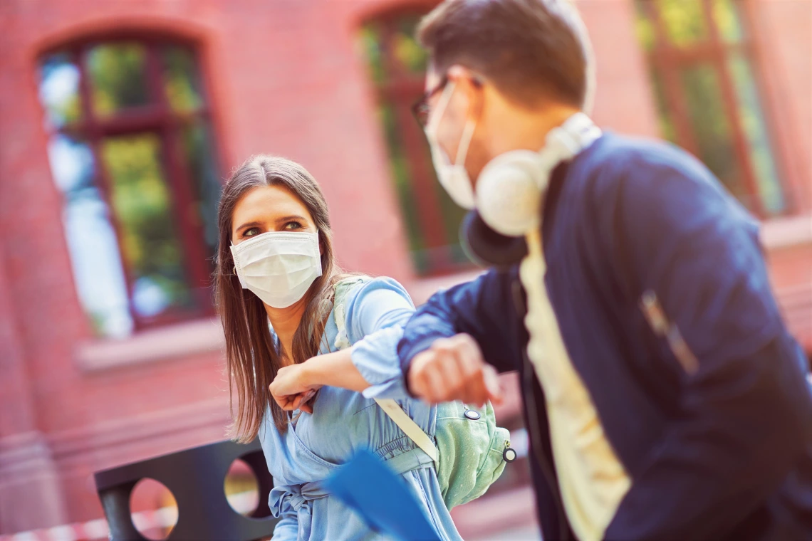 College students in masks elbow bumping on campus